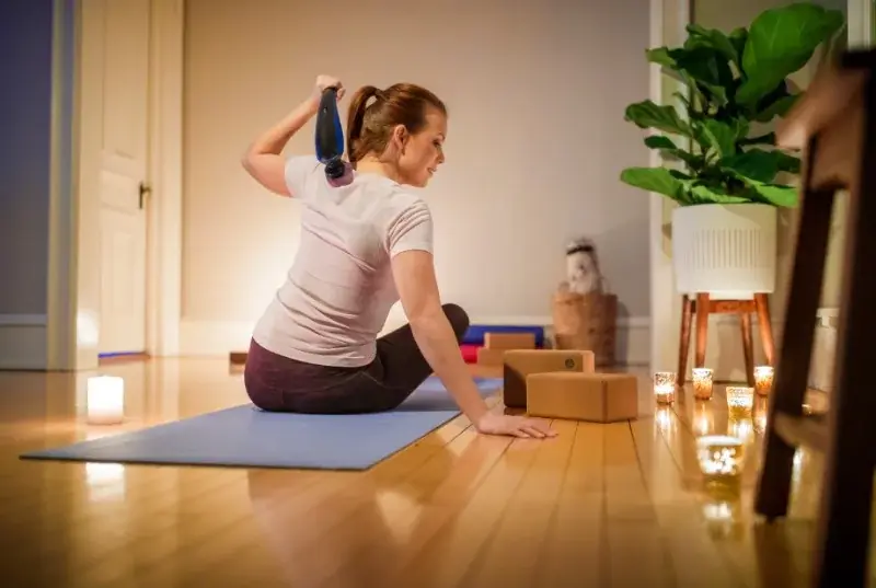 A woman sitting on a yoga mat using a Wahl deep tissue massager.